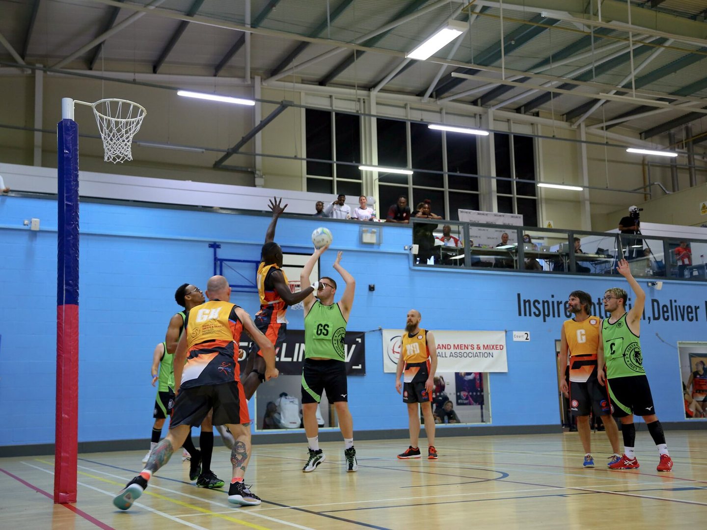Indoor netball match under the post with players jumping for a rebound