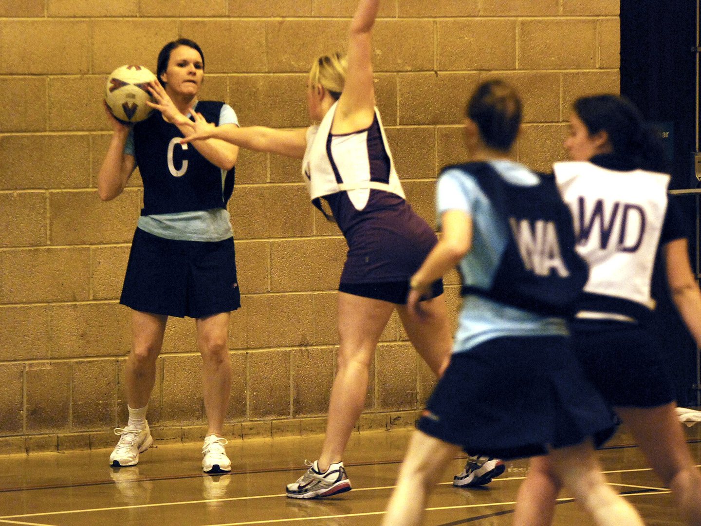 Netball players in action reaching for the ball during a match